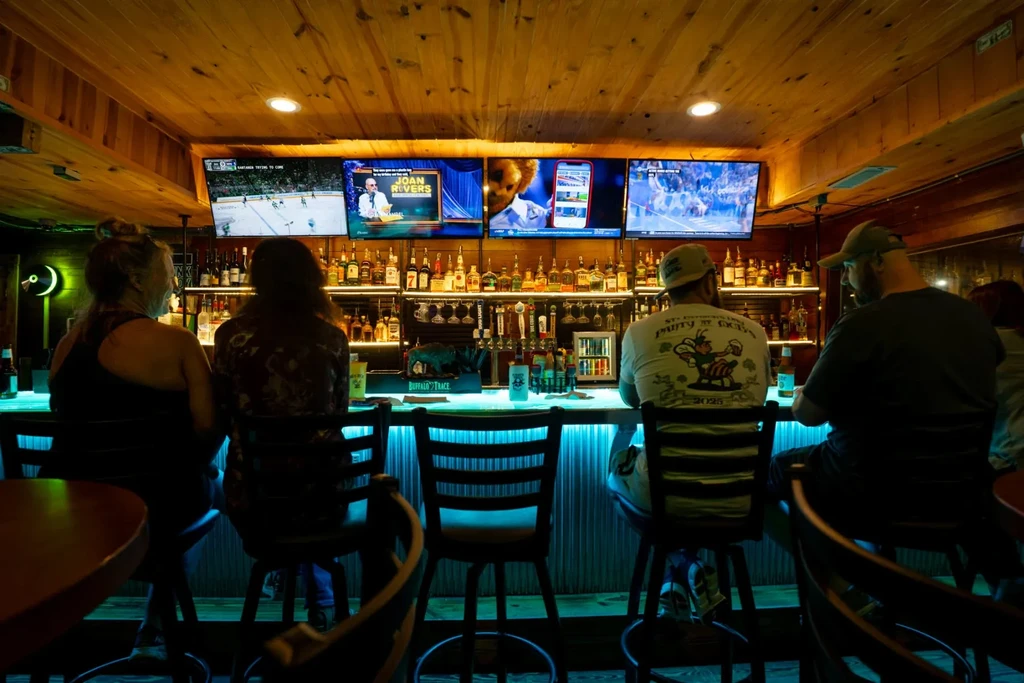 Bar interior with blue neon counter, warm wood, multiple TVs, and patrons.