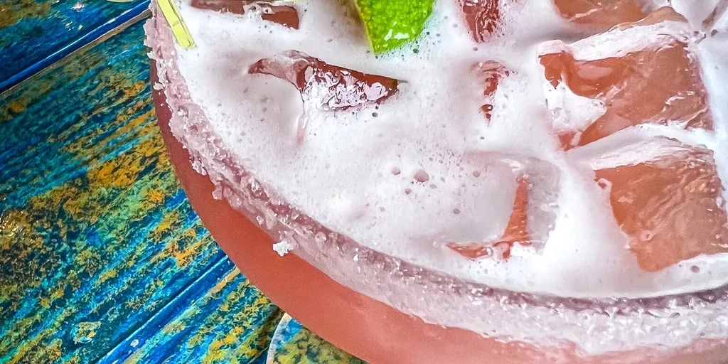 Pink cocktail with lime, sugared rim, on colorful distressed wood.