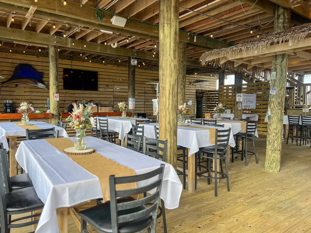 Rustic outdoor event space with high-top tables, floral arrangements, and fish mounts.