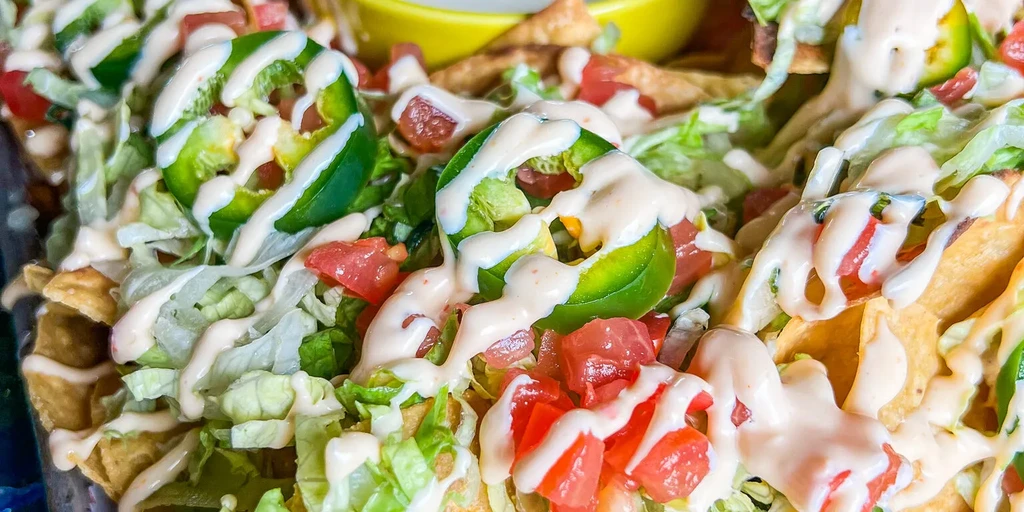 Plate of nachos with lettuce, tomatoes, jalapeños, and creamy sauce.
