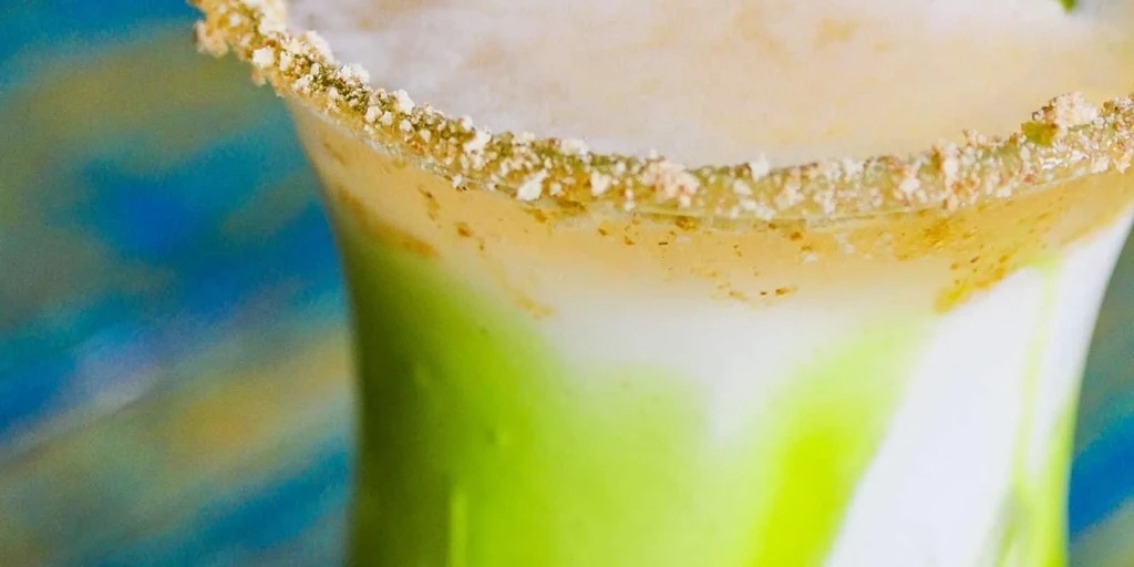 Layered drink: vibrant lime green, creamy white, frothy foam, garnished rim.