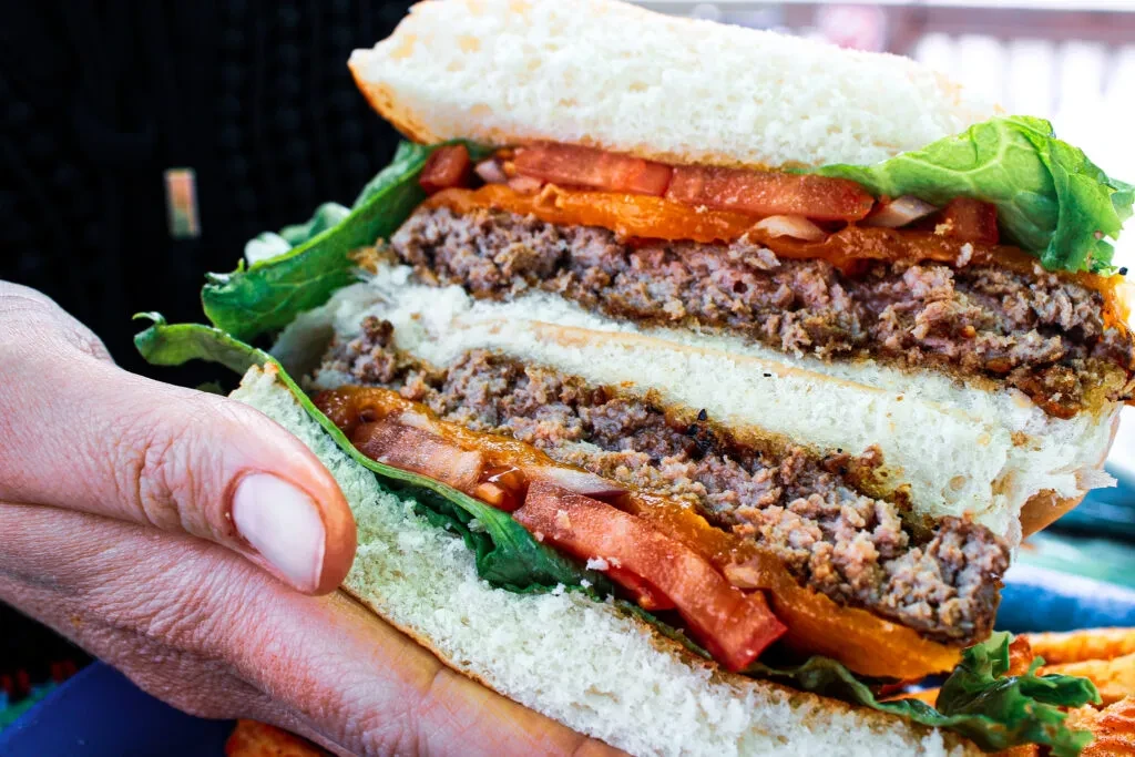 Hand holding a multi-layered burger with lettuce, tomatoes, and fries.