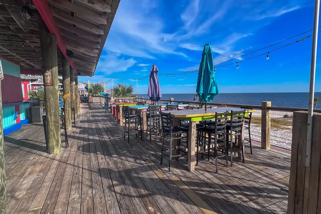 Outdoor waterfront deck bar with colorful tables and umbrellas.