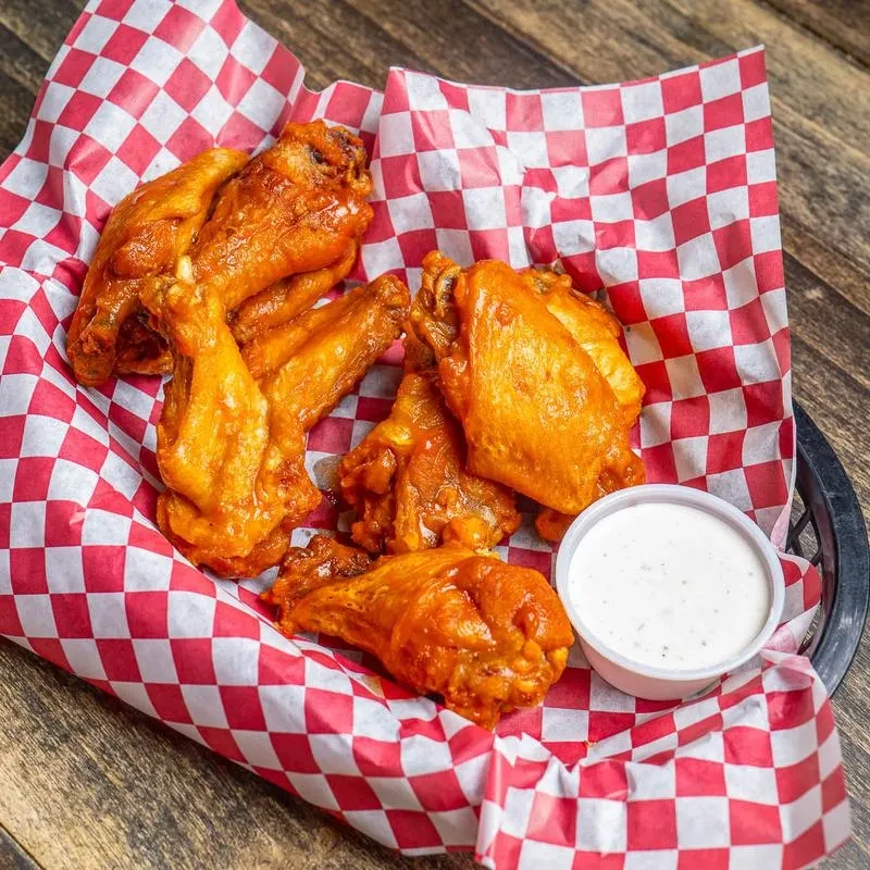 Buffalo wings in a checkered basket with white dipping sauce.