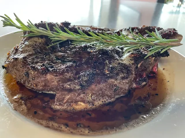 Glistening, thick-cut steak with caramelized crust and rosemary on a white plate.
