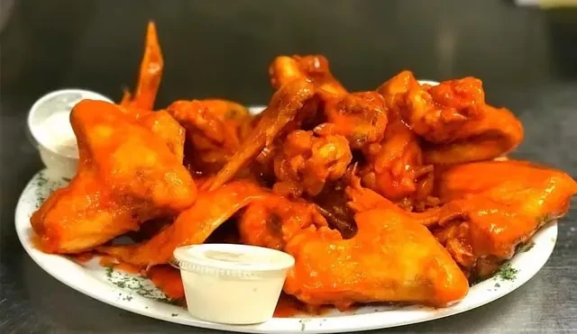 Buffalo wings with vibrant orange sauce, dipping sauce, and herbs.