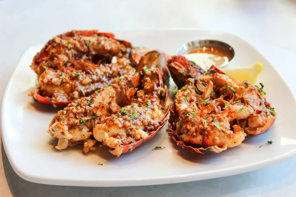Close-up of cooked lobster tails, glistening in garlic-herb sauce, with lemon.