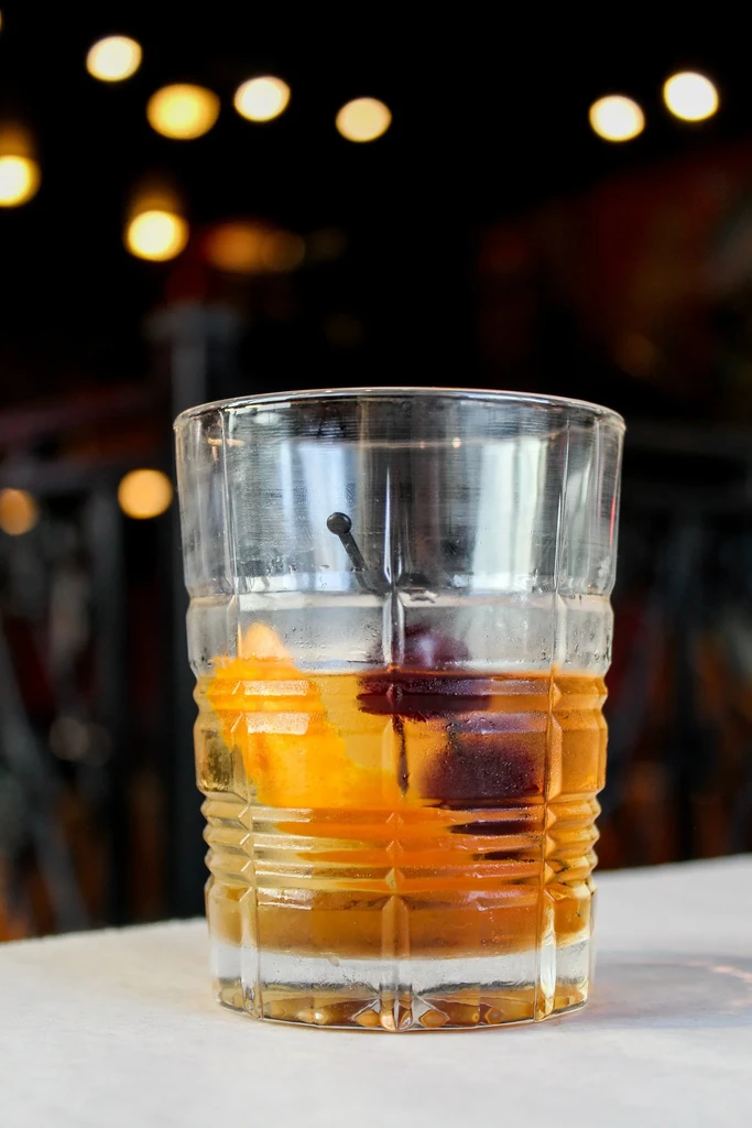 Amber Old Fashioned in faceted glass with orange, cherry, condensation.