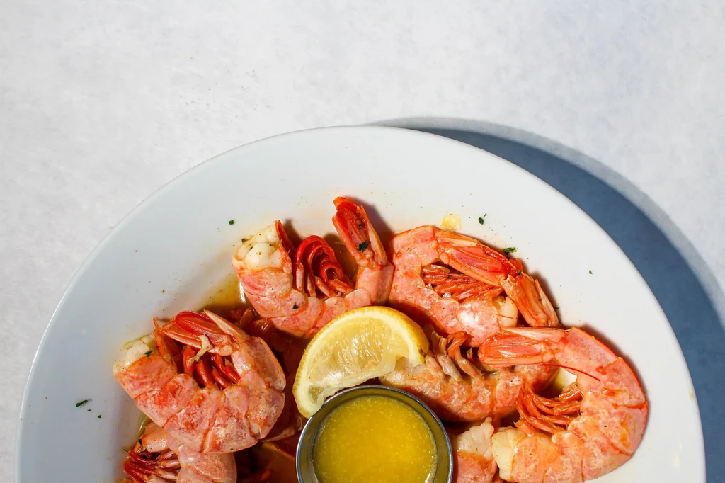 Cooked shrimp with lemon, herbs, and golden sauce on a white plate.
