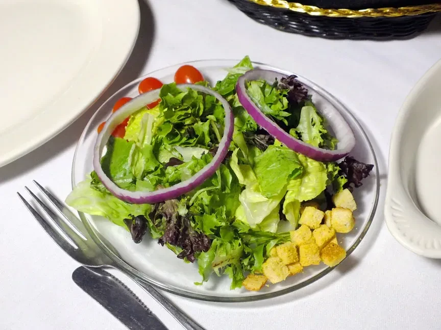 Side salad on glass plate, with lettuce, red onion, tomatoes, croutons.