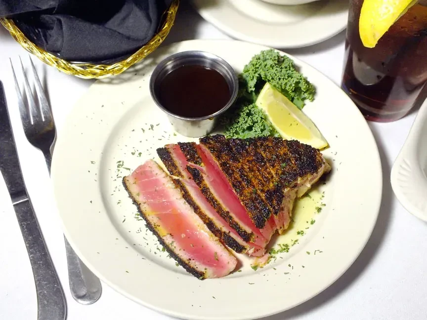 Plated rare seared tuna slices with lemon, kale, and dipping sauce.