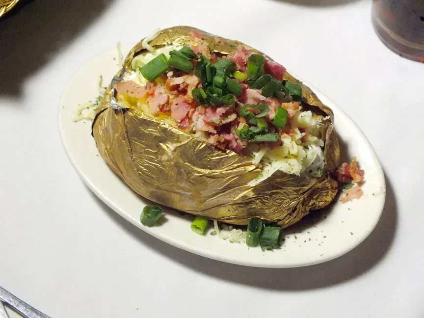 Gold foil baked potato with cheese, bacon, and green onions.