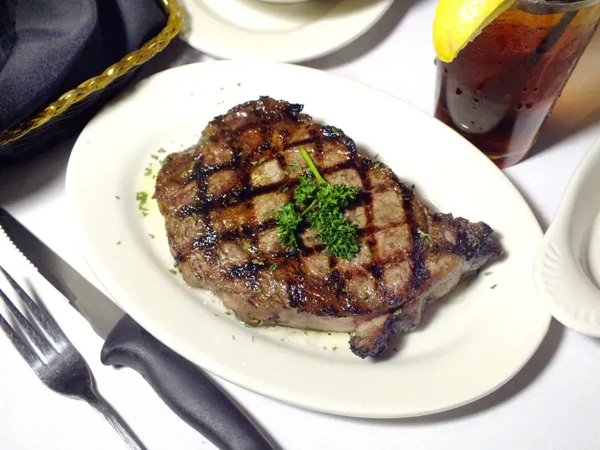 Large grilled steak with prominent grill marks, herbs, and melted butter.