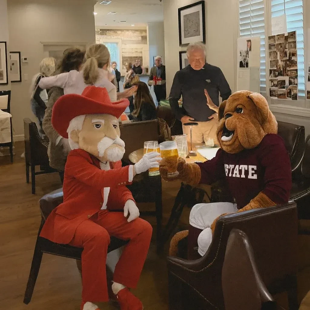 A cowboy mascot and bulldog mascot clink beer glasses at a table.