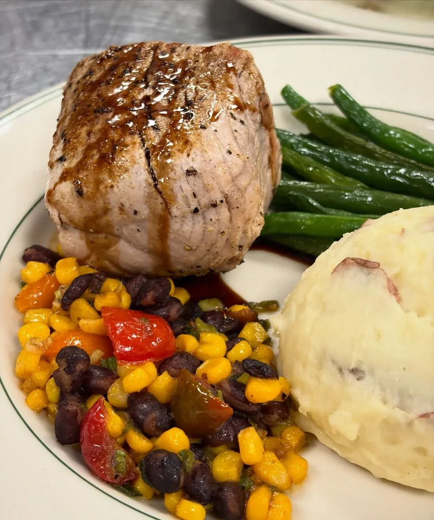 Plated meal with pork, green beans, corn, black beans, and mashed potatoes.