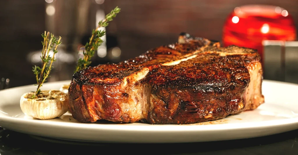 Seared steak with grill marks, roasted garlic, and fresh herbs.