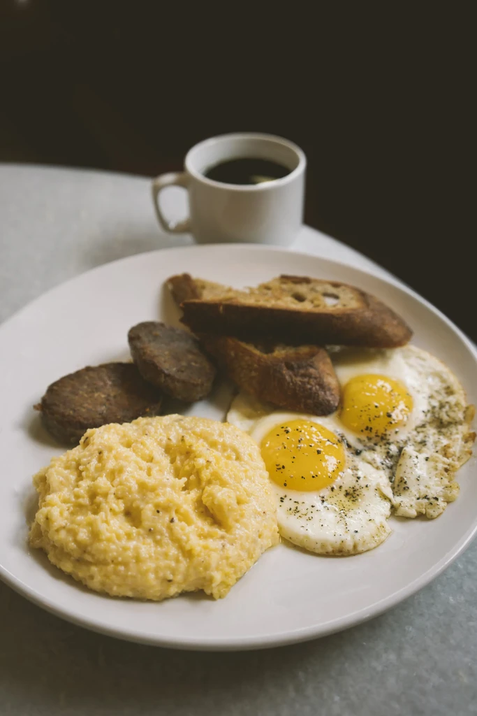 Breakfast plate with grits, fried eggs, sausage, and toasted bread.