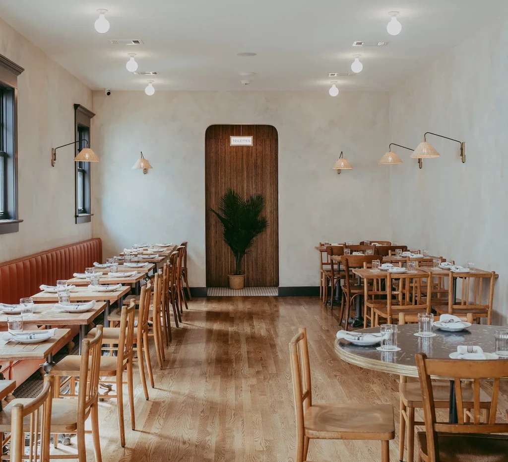Empty modern restaurant with set tables, burnt-orange banquette, and wood.
