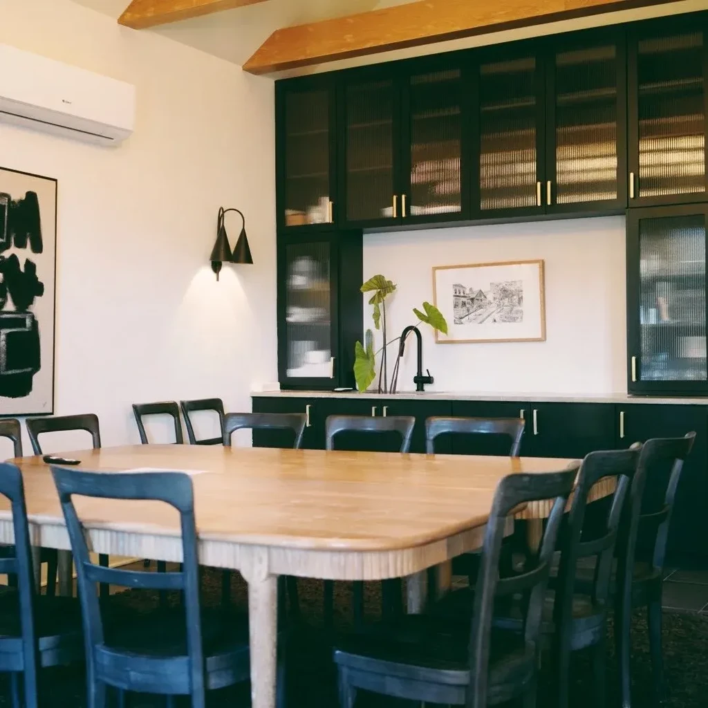 Modern dining room with large wood table, dark chairs, reeded glass cabinet.