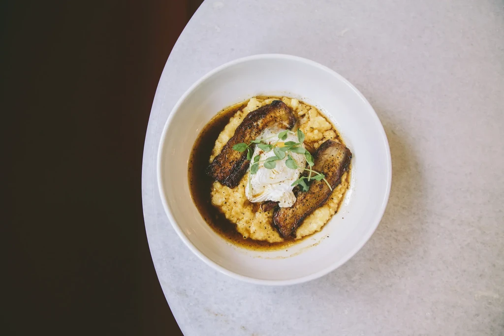 Plated dish: Crispy meat, poached egg, creamy grits, microgreens, sauce.