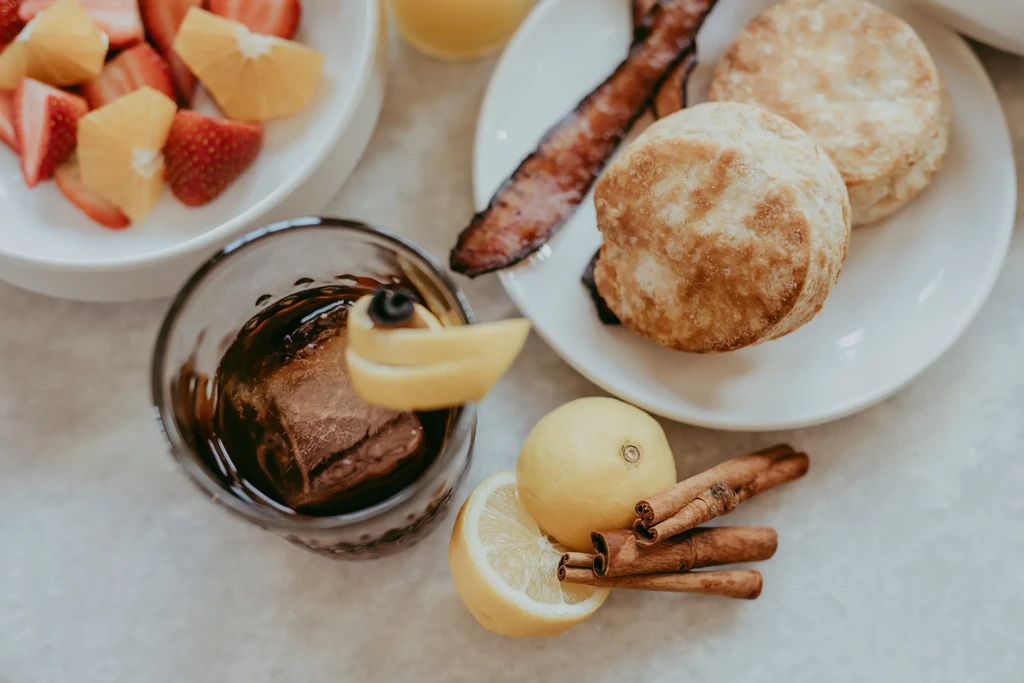 Top-down view of breakfast: fruit, biscuits, bacon, and drinks.