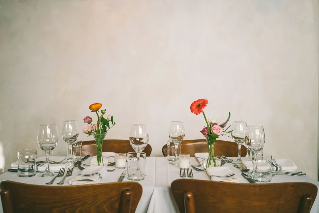 Two elegantly set dining tables with flowers, candles, cutlery, and glassware.