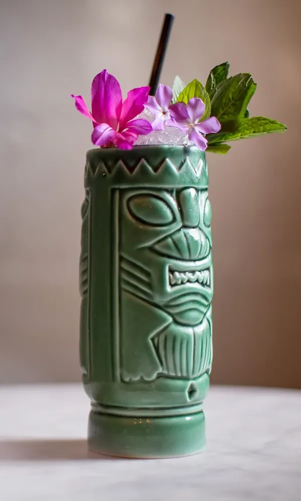 Detailed green tiki mug cocktail with vibrant floral garnishes.