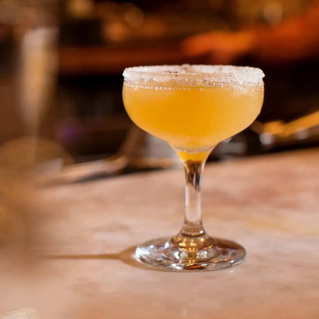 Yellow-orange cocktail in a coupe glass with a sugared rim.