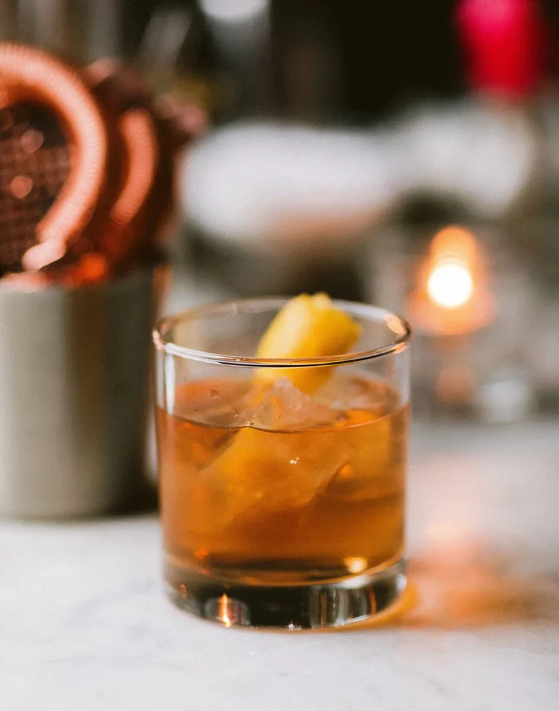 Amber cocktail with ice and large citrus peel in old-fashioned glass.