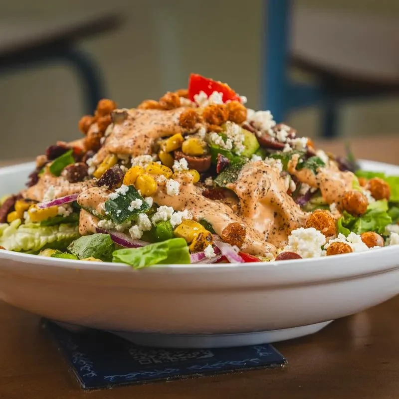 Close-up of a large salad with lettuce, corn, feta, and creamy dressing.