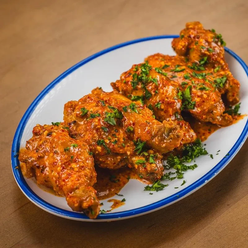 Close-up of chicken wings in spicy orange-red sauce with green herbs.