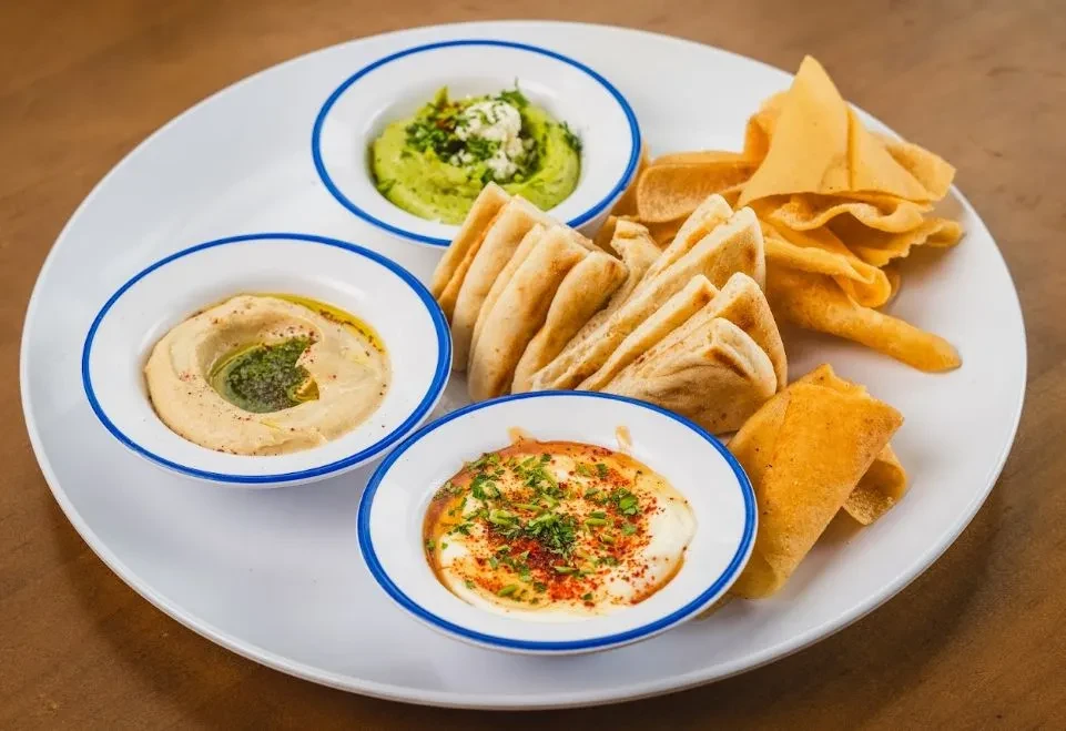 Appetizer platter with three dips, pita bread, and crispy flatbreads.