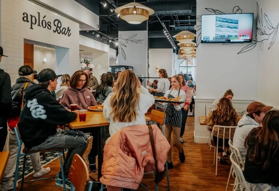 Bustling interior of aplós Bar with diners, server, and modern decor.
