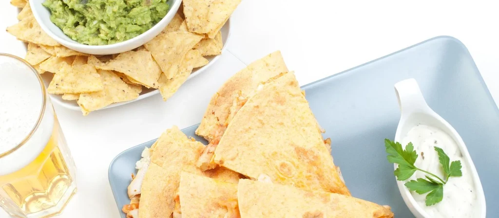 Overhead view of quesadillas, chips, guacamole, sauce, and a golden drink.
