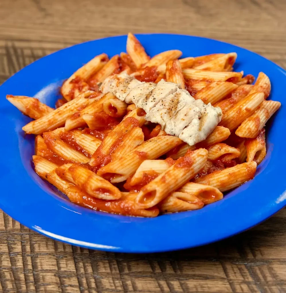 Grilled chicken, penne pasta with red sauce on a blue plate.