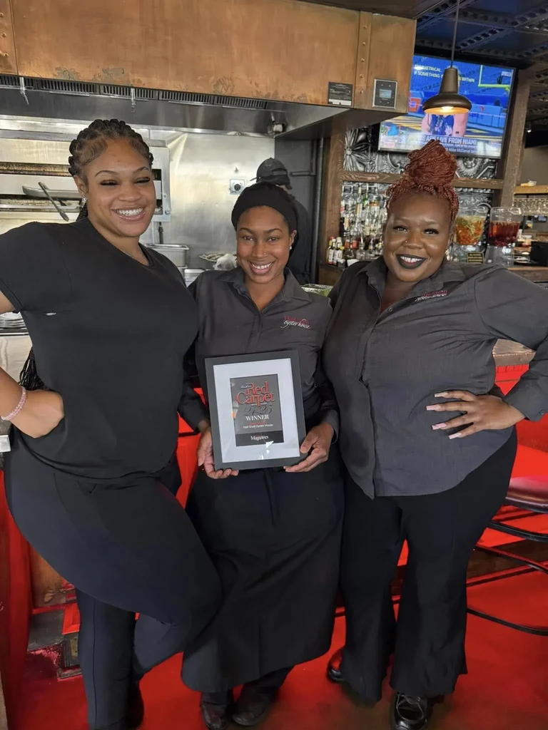 Three smiling staff hold Half Shell Oyster House Red Carpet 2023 award.