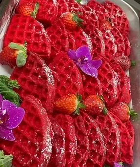 Red triangular waffles, powdered sugar, strawberries, and orchids on a platter.