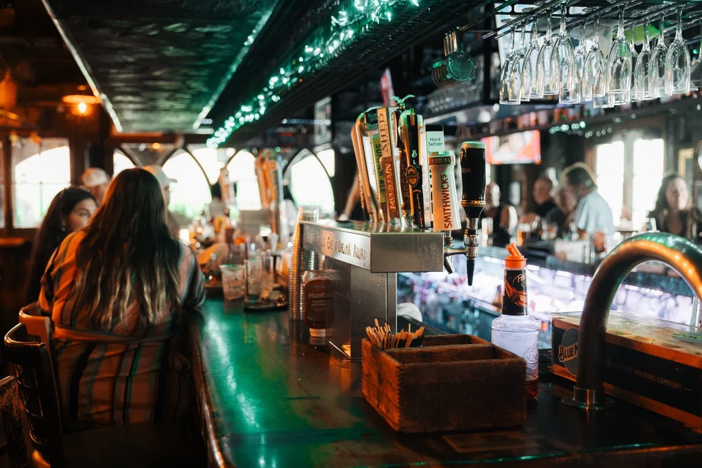 Dimly lit bar with numerous beer taps, hanging glasses, and patrons.
