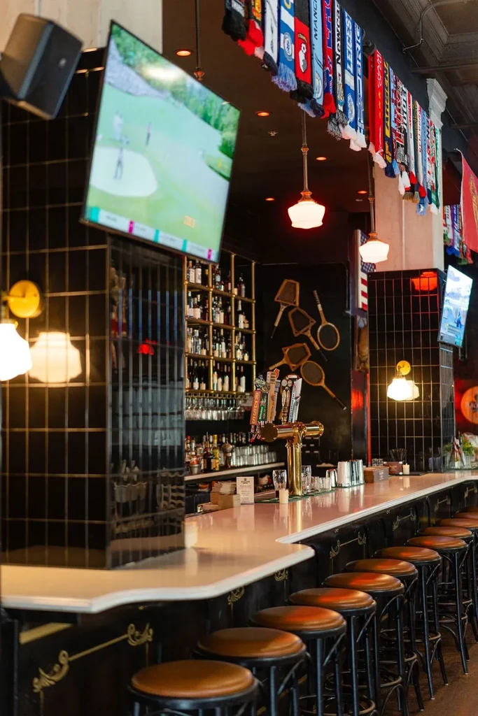 Sports bar interior with curved bar, stocked shelves, TVs, and scarves.