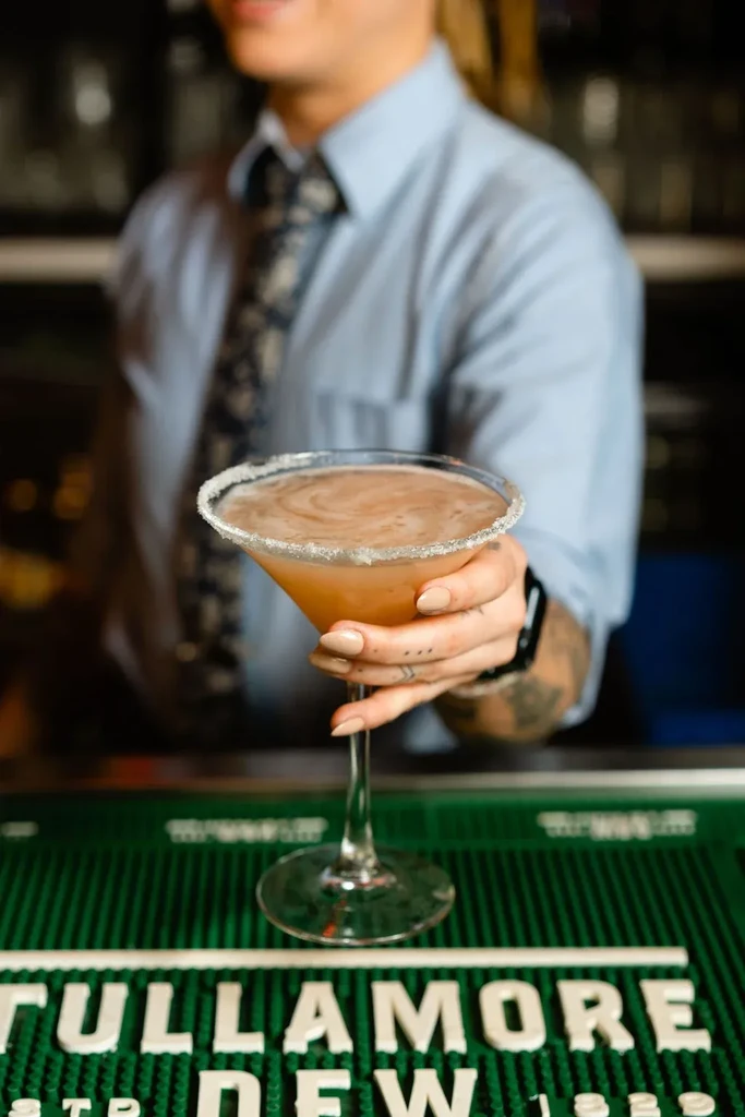 Tattooed hand holds amber cocktail with sugared rim over TULLAMORE DEW mat.