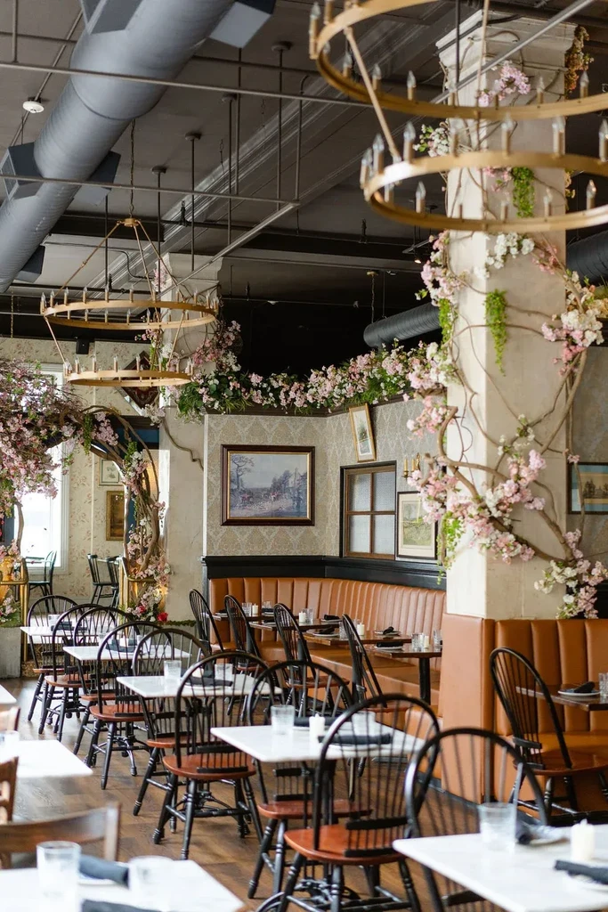 Elegant restaurant interior with marble tables, industrial ceiling, and lush floral decor.