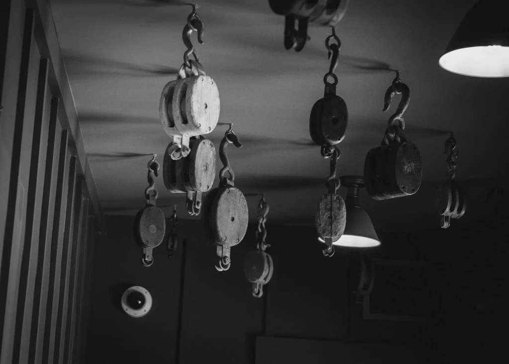 Black and white interior shows many vintage pulleys hanging from ceiling.