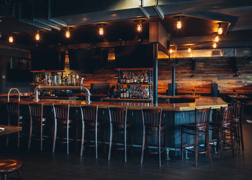 Empty U-shaped wooden bar, stools, liquor bottles, beer taps, industrial lighting.