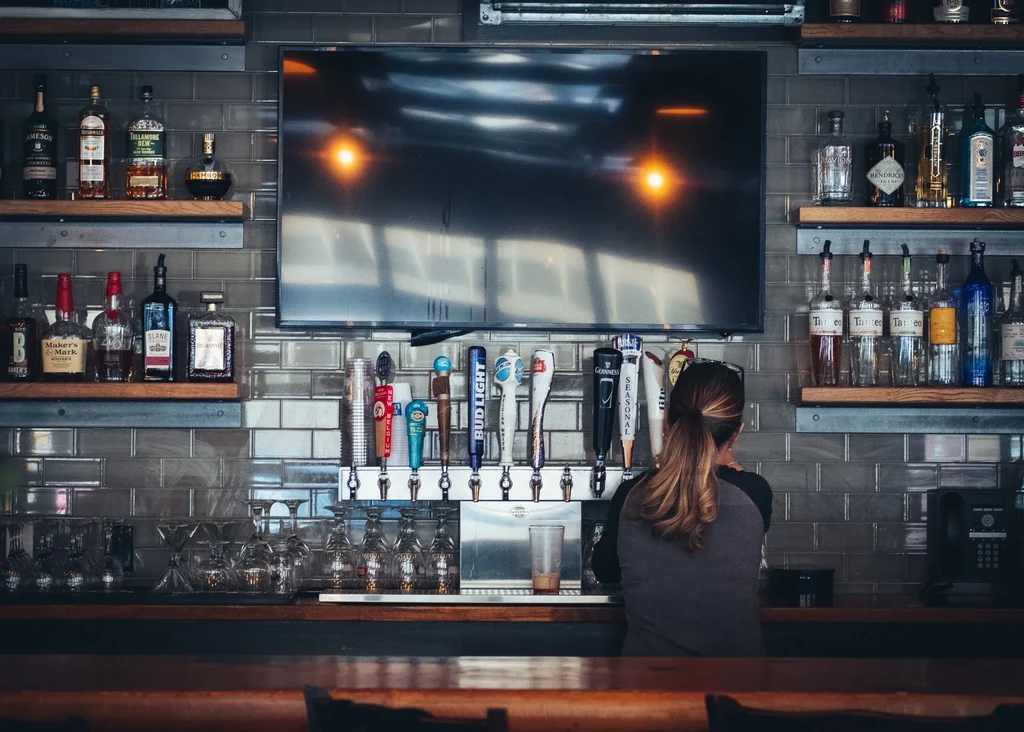 Well-stocked bar with liquor bottles, beer taps, glassware, and a bartender.
