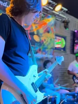 Guitarist plays white electric guitar on stage under blue light.