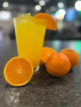 Glass of yellow drink with ice, orange garnish, and fresh oranges.