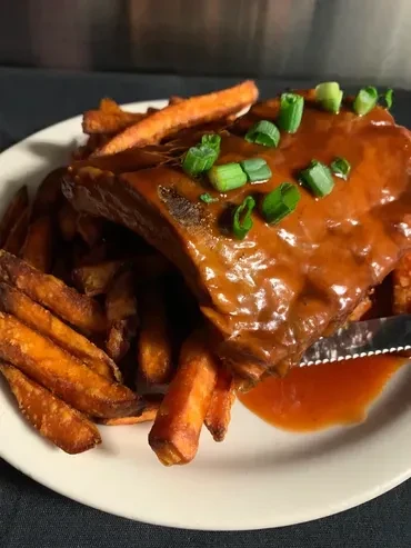 Close-up of sauced BBQ ribs with scallions and sweet potato fries.