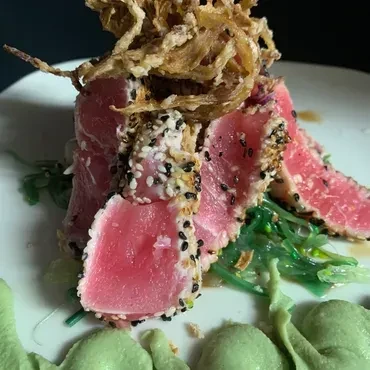 Seared sesame-crusted tuna with crispy onions, seaweed, and green sauce.