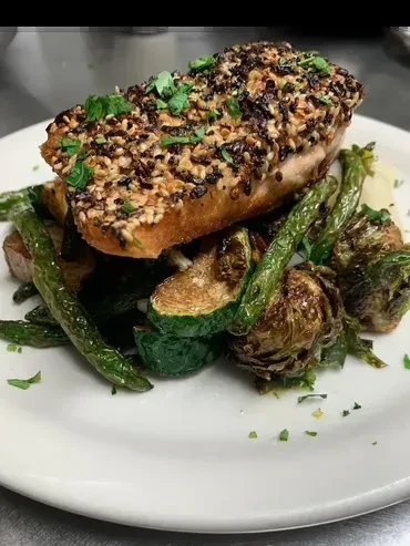 Plated sesame-crusted fish, roasted vegetables, and puree on white plate.