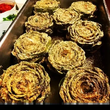 Tray of nine golden-brown baked artichokes, with background garnishes.